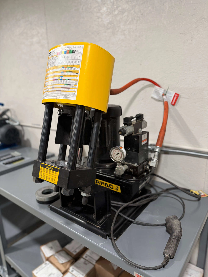 Yellow and black hydraulic press on a gray workbench with a white wall background